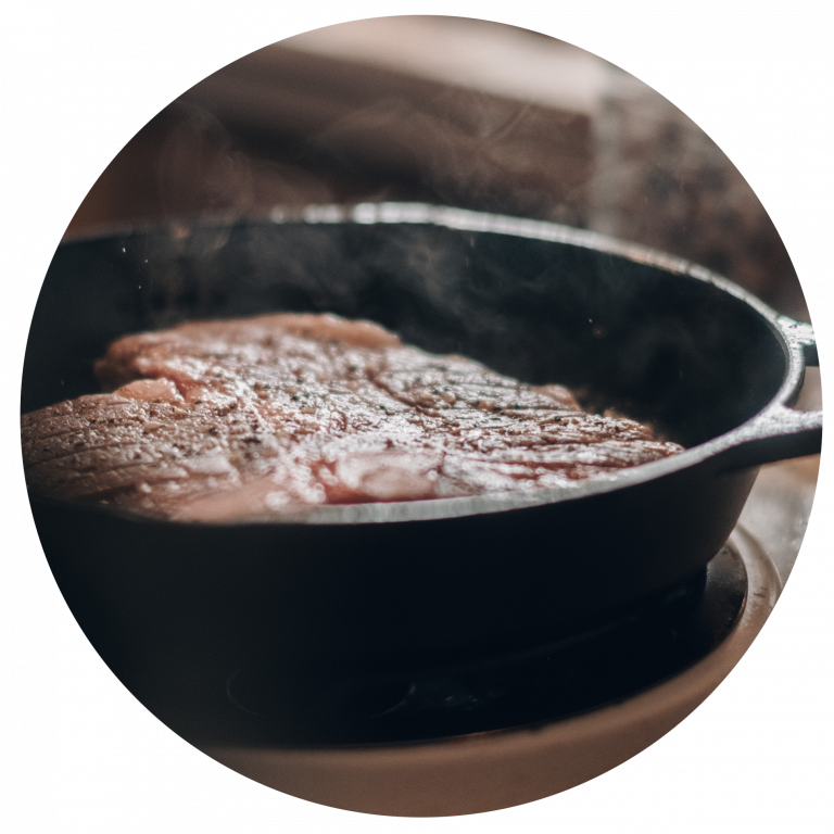 Das Bild zeigt saftige Steaks, die gerade in einer schwarzen Pfanne gebraten werden.